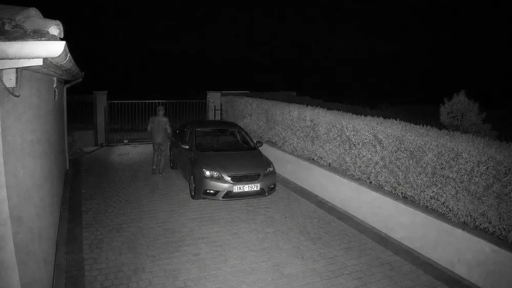 Σκηνή επίδειξης, νυχτερινή λήψη με υπέρυθρο: αυτοκίνητο μπροστά στην αυλόπορτα και κάποιος που περπατά δίπλα του.